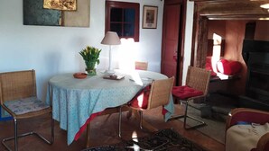 Ein gemütliches Wohnzimmer mit rundem Tisch, zwei Stühlen, einem gemusterten Teppich, einer Hängelampe und einem Kamin.