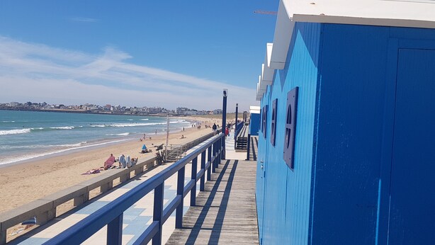 A pier leading to a beach with a clear view of the ocean and a distant shoreline.
