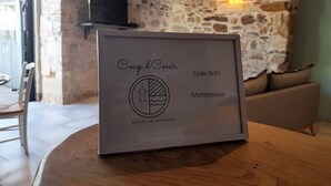 A framed sign with text and a logo on a wooden table in a room with stone walls and a television on a shelf.