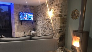 A cozy living room with a stone wall, a sofa, a TV, and a wood-burning stove.