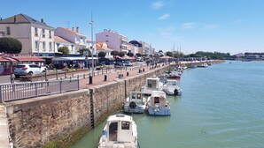 A waterfront promenade with boats docked along the quay, a stone wall, and buildings with shops and restaurants.