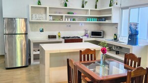 A modern kitchen with a central island, wooden chairs, a stainless steel refrigerator, and a ceiling fan. - Hotel & Suites Oasis Bacalar "Suite Toucan" (Bacalar)