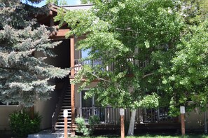 A residential building with a wooden staircase leading to a balcony, surrounded by lush greenery. - Crestview Condo 25 by Alpine Lodging Sun Valley (Ketchum)