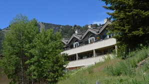 Un edificio de varios pisos con balcones, rodeado de árboles y un paisaje montañoso.