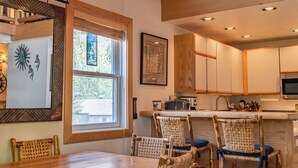 A kitchen with wooden cabinets, a dining table, wicker chairs, and a window with a view of trees.