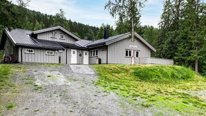 A two-story building with a sloped roof, a gravel driveway, and a forested backdrop. - Stunning apartment in Hemsedal (Hemsedal)
