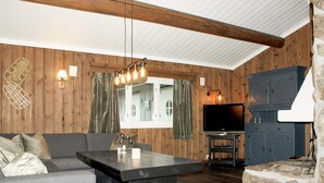 A cozy living room with a wooden interior, a sofa, a coffee table, a TV, and a stone fireplace. - Stunning apartment in Hemsedal (Hemsedal)