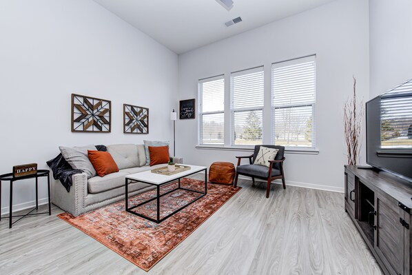 A modern living room with a sofa, coffee table, and armchair, a flat-screen TV, and a large window with blinds. - *LUXURY WALK IN THE PARK-2* (Fishers)