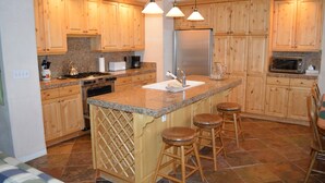 A kitchen with wooden cabinets, granite countertops, stainless steel appliances, and bar stools. - River Ridge Townhome 20 by Alpine Lodging Sun Valley (Ketchum)