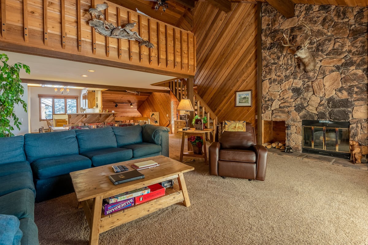 Una sala de estar acogedora con chimenea de piedra, techo de madera y un ventanal grande.