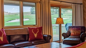 Una habitación con sofá y sillón de cuero, una mesa de centro de madera y vistas a un campo de golf a través de grandes ventanales.