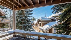 Una terraza de madera con barandas cubiertas de nieve y vistas a edificios y árboles cargados de nieve.