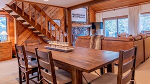 Una mesa de madera para comer con sillas, una chimenea, un sofá y una escalera.