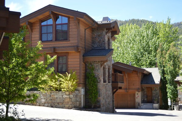 A two-story log cabin with a stone foundation, large windows, and a covered front porch. - Skiview Townhome 3C by Alpine Lodging Sun Valley (Ketchum)