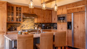 A kitchen with wooden cabinets, a granite countertop, a stainless steel refrigerator, and pendant lighting.