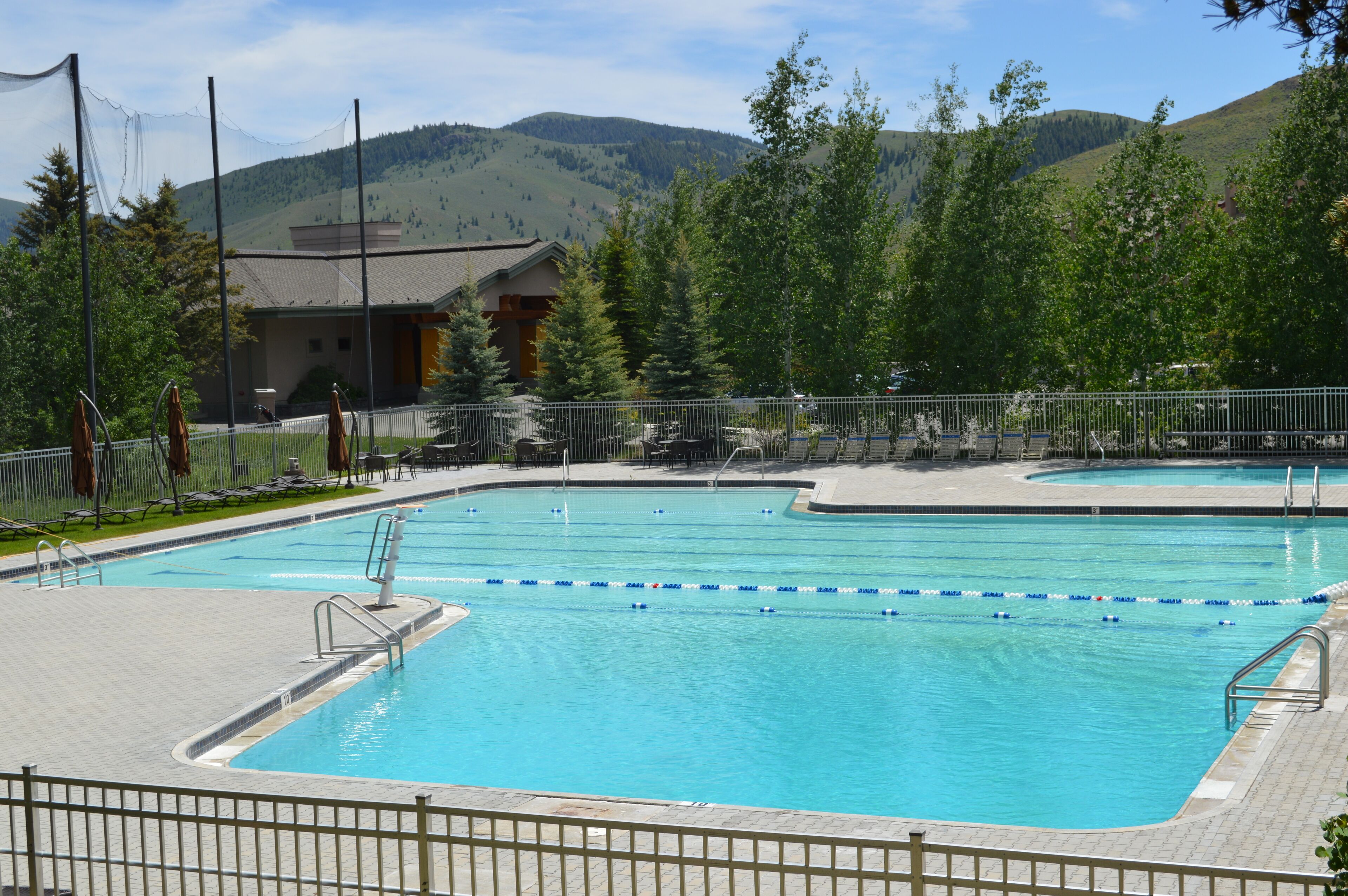 A rectangular swimming pool with a tiled deck, surrounded by a metal fence.