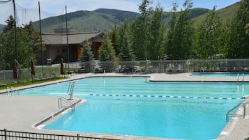 A rectangular swimming pool with a tiled deck, surrounded by a metal fence.