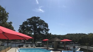 Una piscina con sombrillas rojas, sillones de descanso y una fuente.