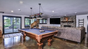 Ein Billardtisch, ein Hund, ein Kamin aus Stein und ein großer Fernseher an der Wand.