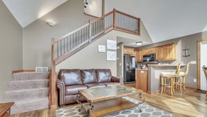 A spacious living area with a brown leather sofa, a wooden coffee table, and a staircase leading to an upper level.