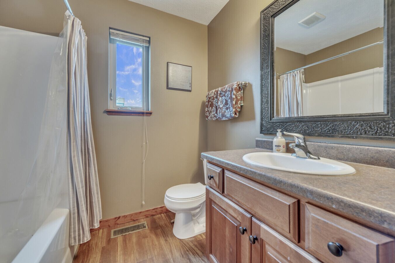 A bathroom with a shower, toilet, vanity with a sink, and a large mirror.