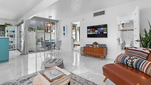 A spacious living area with a sofa, coffee table, and a dining set. A TV is mounted on the wall, and there is a sliding glass door leading to a patio. - Bohemian Mid-Century at the Famed Ocotillo Lodge (Palm Springs)