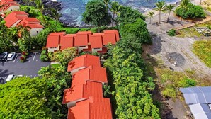 A coastal hotel with red-roofed buildings, a parking area, and a beach with palm trees. - Keauhou Kona Surf & Racquet Club #1-103 (Kailua-Kona)
