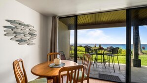 A dining area with a wooden table and chairs, a decorative fish wall art, and a view of the ocean through large sliding glass doors. - Keauhou Kona Surf & Racquet Club #1-103 (Kailua-Kona)