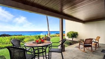 A covered patio with a table set for two, chairs, and a view of the ocean.