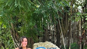 Une femme se tient à côté d’un panneau indiquant « Suites Oasis Bacalar ».