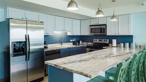 A modern kitchen with stainless steel appliances, a marble countertop, and green chairs.