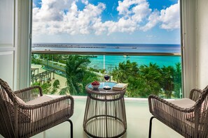 A balcony with wicker chairs, a small table with a glass of wine, and a view of the ocean and beach.