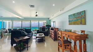 A spacious living room with a large window overlooking the ocean, a wooden dining table, and a cozy seating area.