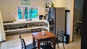 Een moderne keuken met een eethoek, met een houten tafel, zwarte stoelen, een koelkast en een plafondventilator.