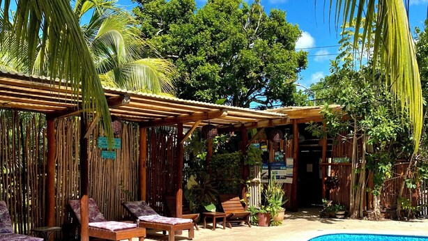 Una piscina con borde de azulejos, rodeada de sillones de madera y una pérgola de bambú.