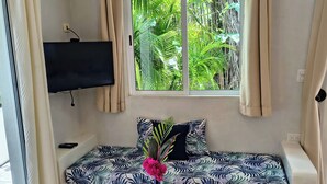 Una sala de estar con un sofá, una mesa de centro, un televisor montado en la pared y una ventana con cortinas.