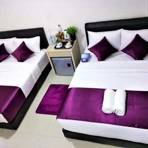 Habitación de hotel con dos camas, cada una con una colcha morada y almohadas a juego. Hay una mesita de noche pequeña con una planta y una botella de agua.