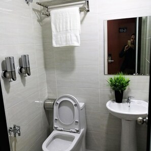 Un baño con inodoro, lavamanos, toallero y espejo.