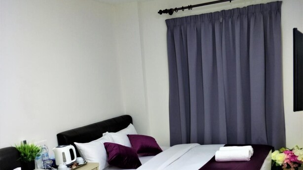 A hotel room with two beds, each with white bedding and purple accents, a nightstand with a kettle, a small plant, and a vase with flowers. - Citi Hotel @KL Sentral (Kuala Lumpur)