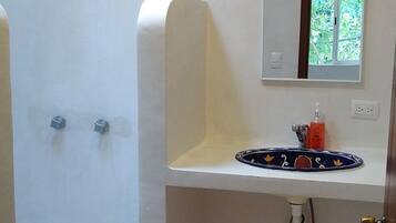 Un baño con ducha, lavabo y espejo, y suelo de baldosas.
