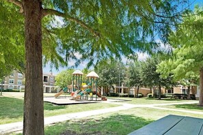 Enjoy a serene park setting with a playground, surrounded by mature trees and residential buildings.