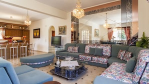 A spacious living area with a sofa set, a coffee table, and a TV. There is a kitchen area with wooden cabinets and a dining space with chairs. - Harmony Country House-Live in the Nature (Archanes-Asterousia)
