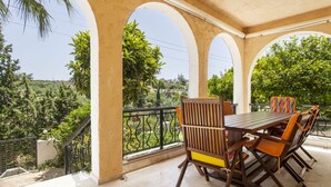 A covered outdoor dining area with a table and chairs, surrounded by a railing with a view of greenery and hills. - Harmony Country House-Live in the Nature (Archanes-Asterousia)