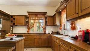 A kitchen with wooden cabinets, a tiled floor, a window with curtains, and a fruit bowl on the counter. - Harmony Country House-Live in the Nature (Archanes-Asterousia)