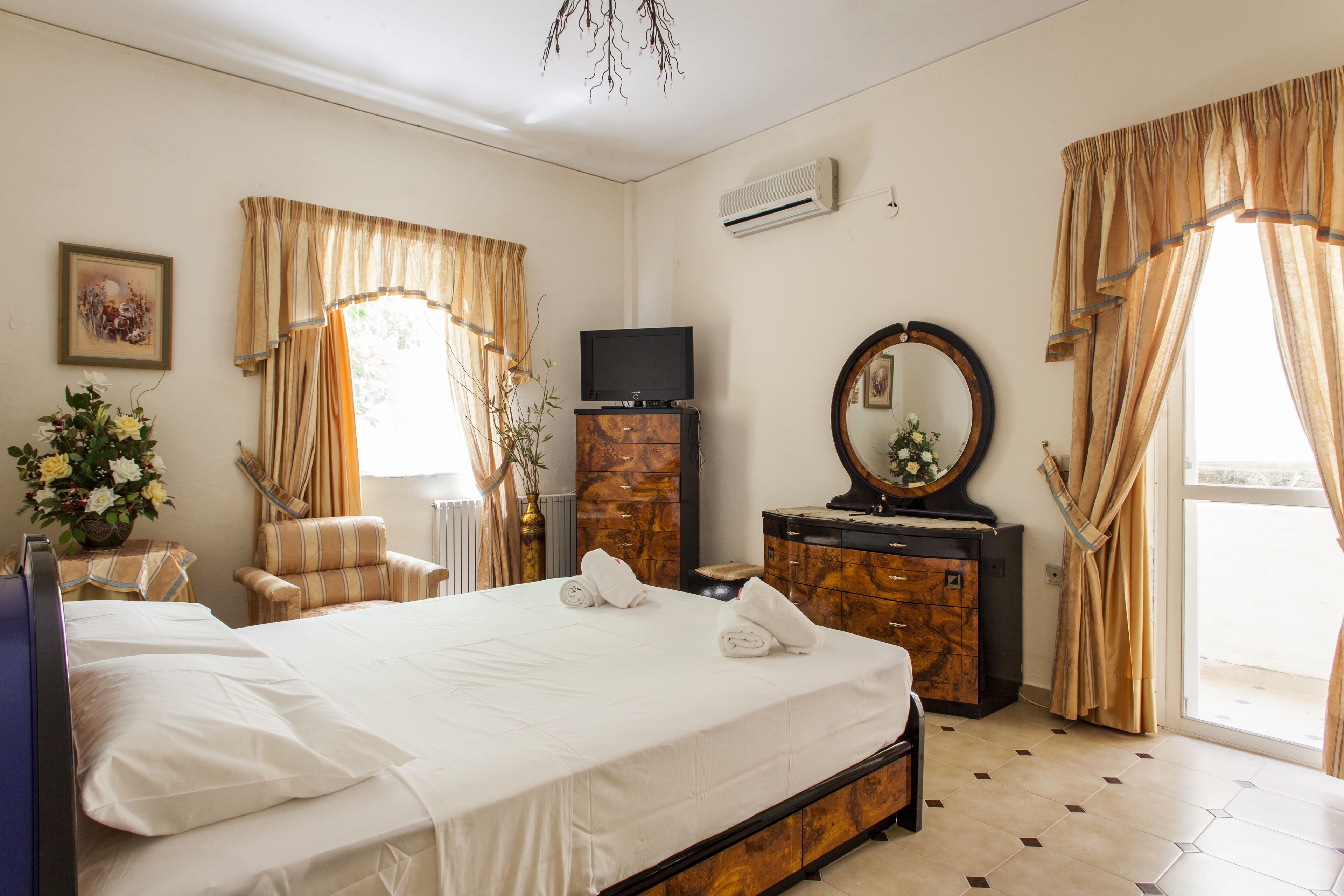 Une chambre d’hôtel avec un grand lit, une télévision, une commode, un miroir et des rideaux.