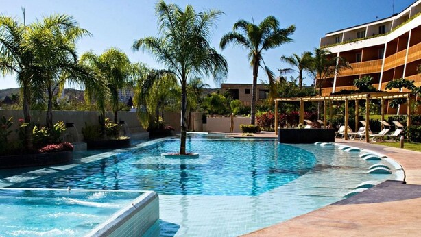 Piscina com borda azulejada, cercada por palmeiras e cadeiras de descanso.