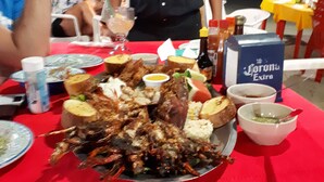 Uma mesa de jantar com diversos pratos, incluindo frutos do mar e arroz, e uma garrafa de cerveja Corona Extra.