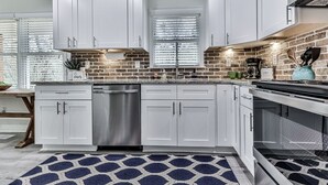 A modern kitchen with white cabinets, a stainless steel dishwasher, a brick backsplash, and a patterned rug. - Fully Renovated Ranch Home 1/2 mi from Charming downtown Ball Ground (Ball Ground)