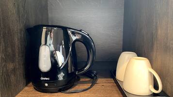 A black electric kettle with a digital display, two white mugs, and a wooden shelf.