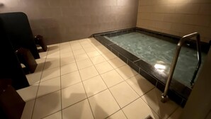 Ein Wellnessbereich mit Whirlpool, gefliestem Boden und Holzbalkendecke.